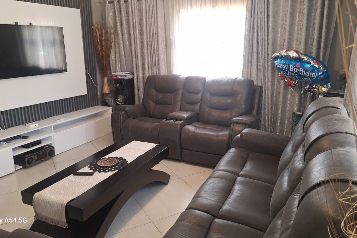 A well-maintained living room featuring tiled flooring, a modern feature wall with built-in media cabinetry, and large windows with curtains.
