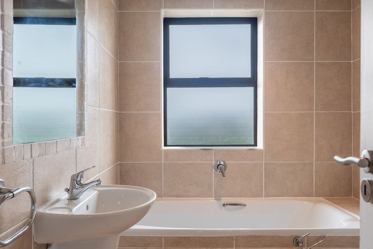 A clean, well-maintained bathroom featuring a pedestal basin, built-in bathtub, and neutral wall tiling with a frosted window for natural light.