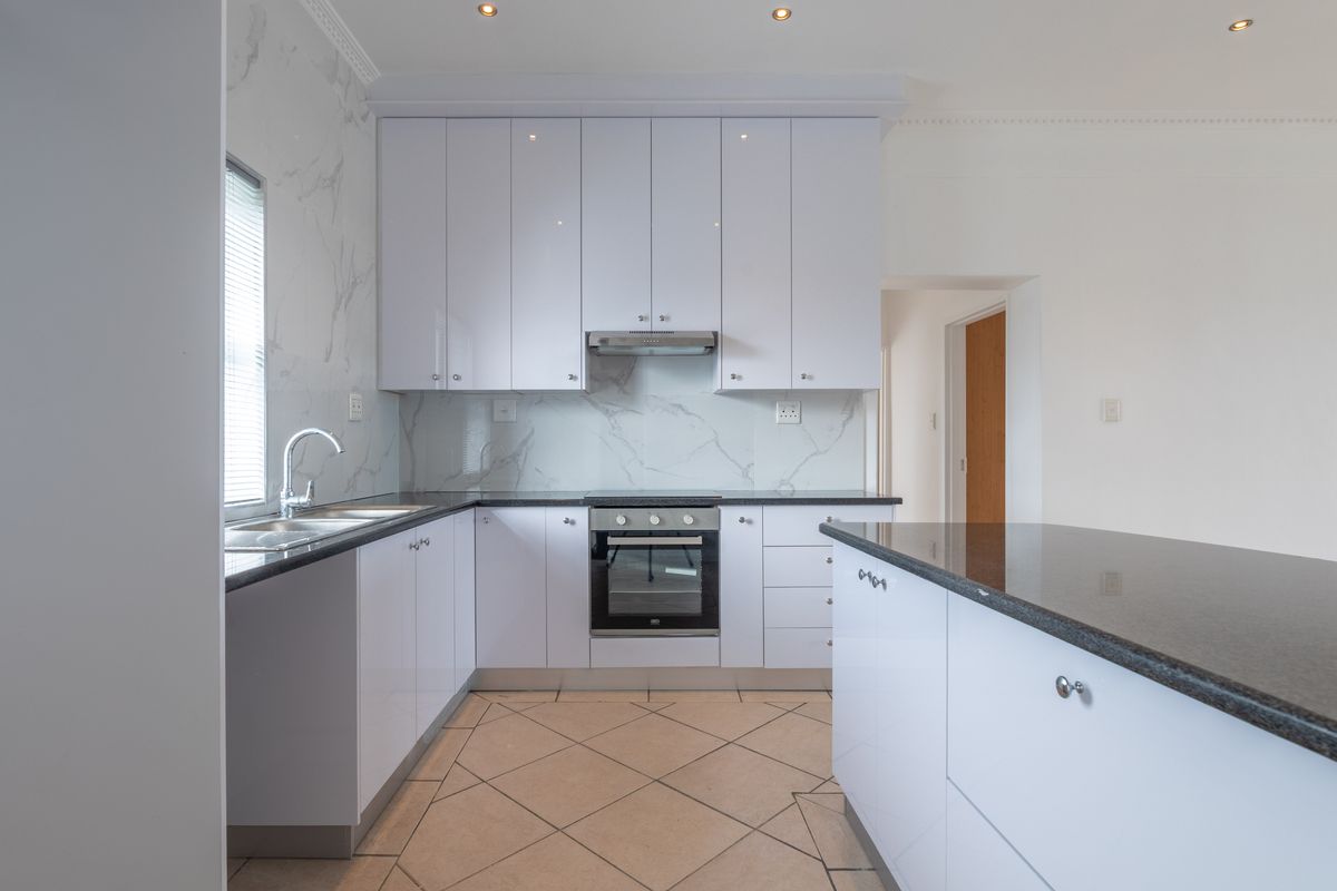 Modern kitchen featuring white cabinetry, dark stone countertops, marble-look splashback, built-in oven, extractor fan, and a functional kitchen island.