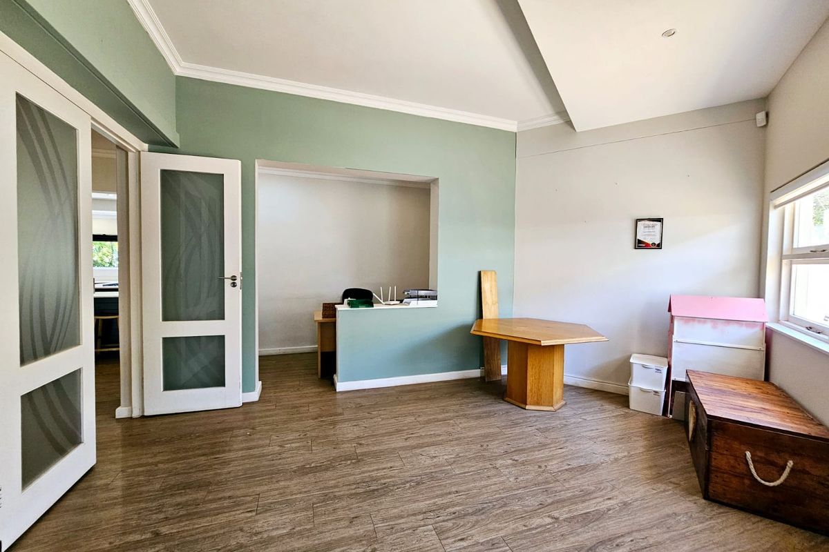 A bright living area featuring laminate flooring, decorative cornice, and a convenient pass-through window connecting to an adjacent space.