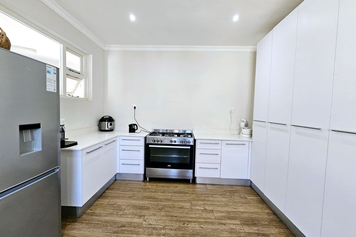 Modern kitchen featuring white cabinetry, stone countertops, stainless steel oven with gas hob, and wood-look laminate flooring.