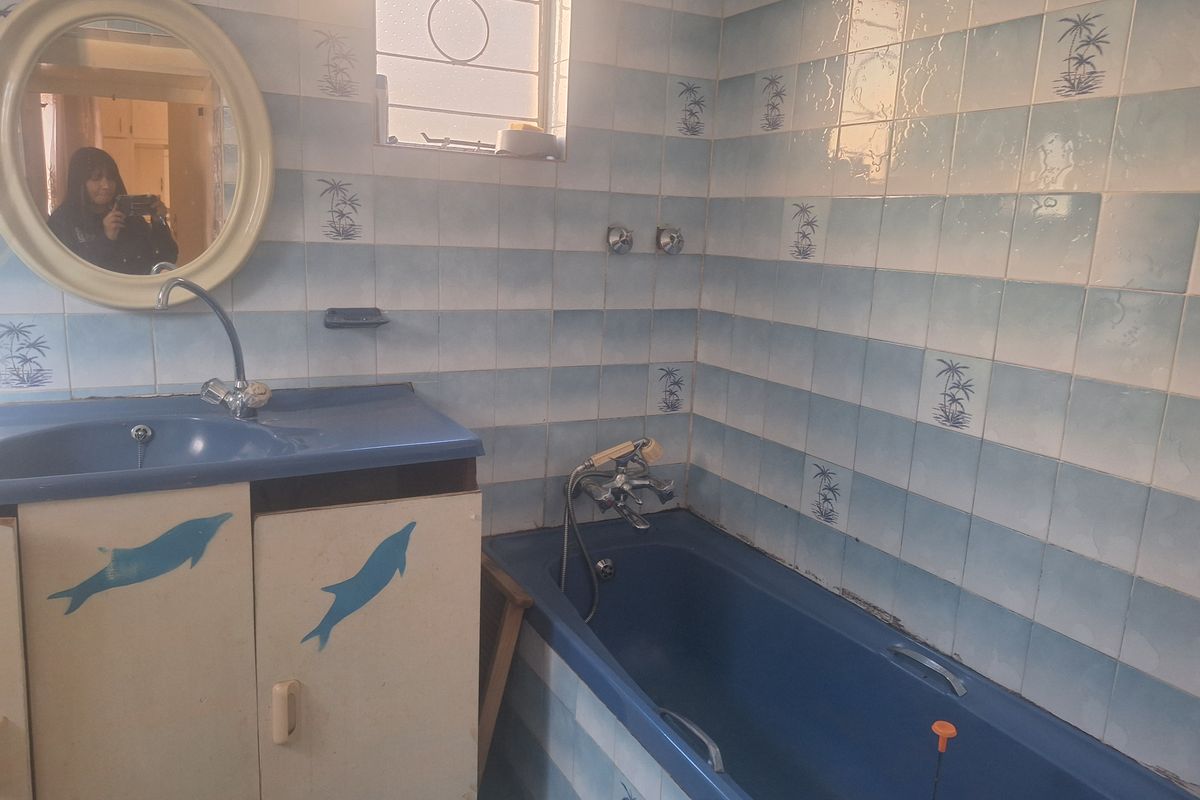 A dated bathroom featuring blue sanitary ware, a built-in bathtub, and patterned wall tiling.