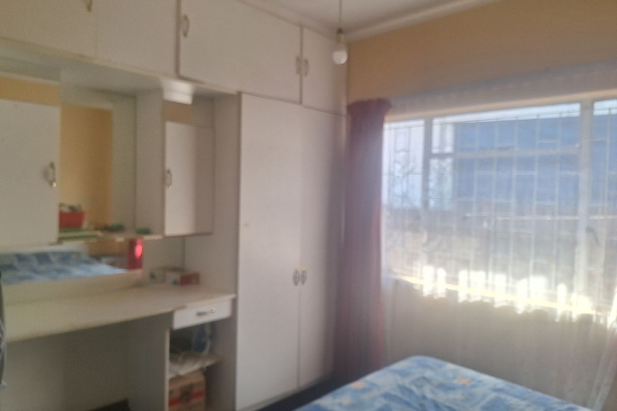 A bedroom featuring built-in cupboards with an integrated vanity unit and security bars on the window.
