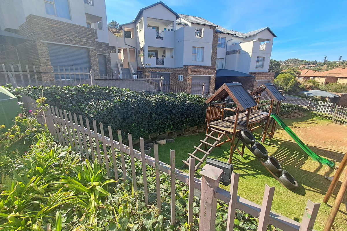 Rear view of the townhouse complex featuring a communal garden area, retaining walls, metal fencing, and multi-level residential units with balconies.