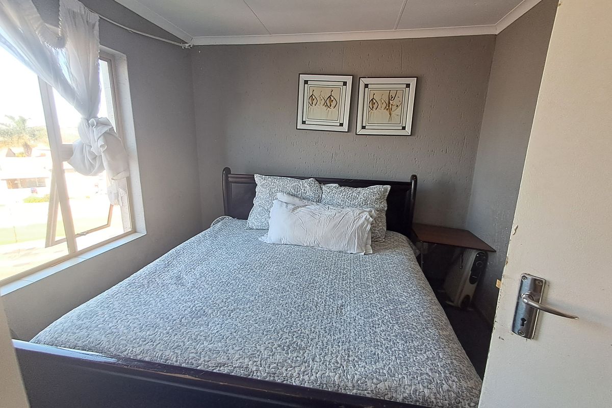A compact bedroom featuring textured walls and an aluminium window frame, providing a functional space with potential for cosmetic updates.