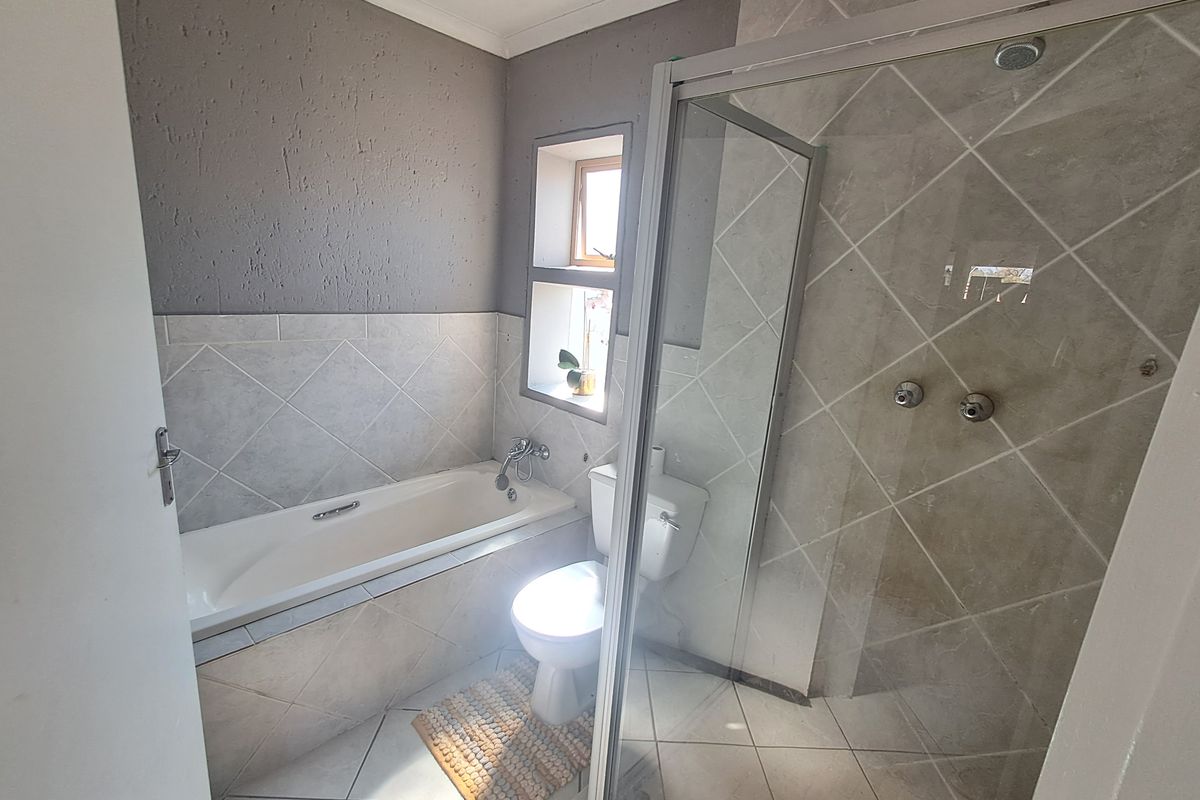 A functional bathroom featuring a built-in bathtub, a separate glass-enclosed shower, and neutral tiled finishes throughout.