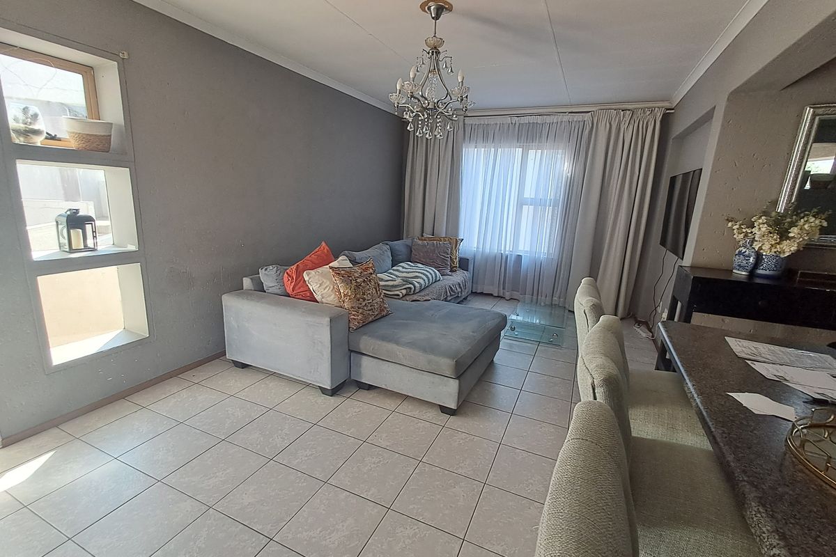 A living room featuring tiled flooring, recessed wall shelving, and a central chandelier, offering a functional space with potential for cosmetic updates.