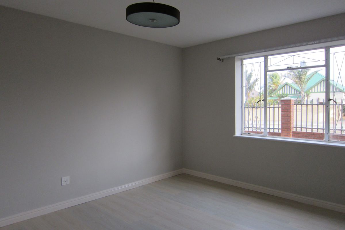 A clean, empty bedroom featuring neutral walls, light-toned flooring, and a window with security bars, providing a bright and versatile living space.