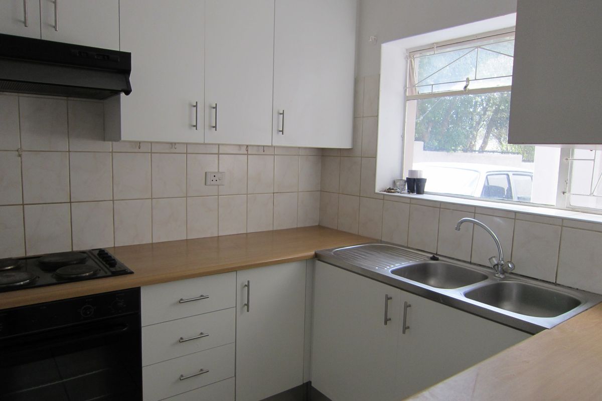 A functional kitchen featuring white cabinetry, laminate countertops, a double stainless steel sink, and built-in electric cooking appliances with tiled splashbacks.