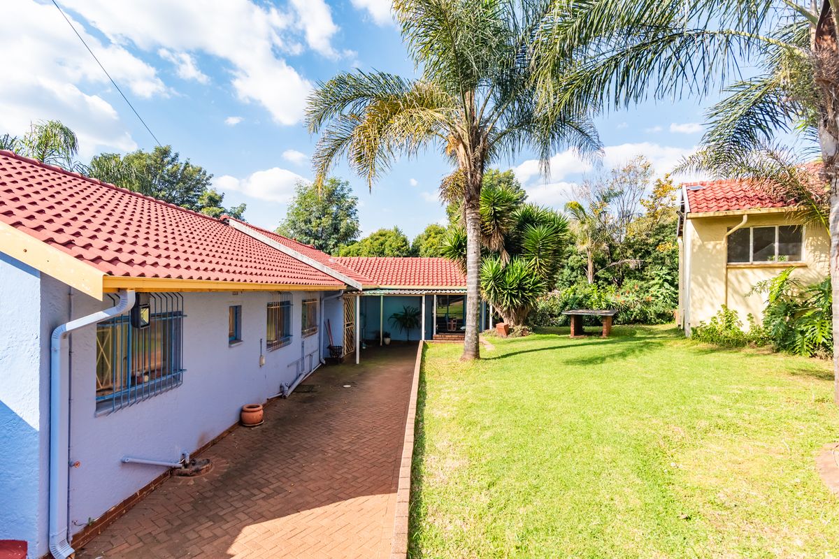 Rear view of the property featuring a paved walkway, lawn area, and tiled roof structure with security bars on windows.
