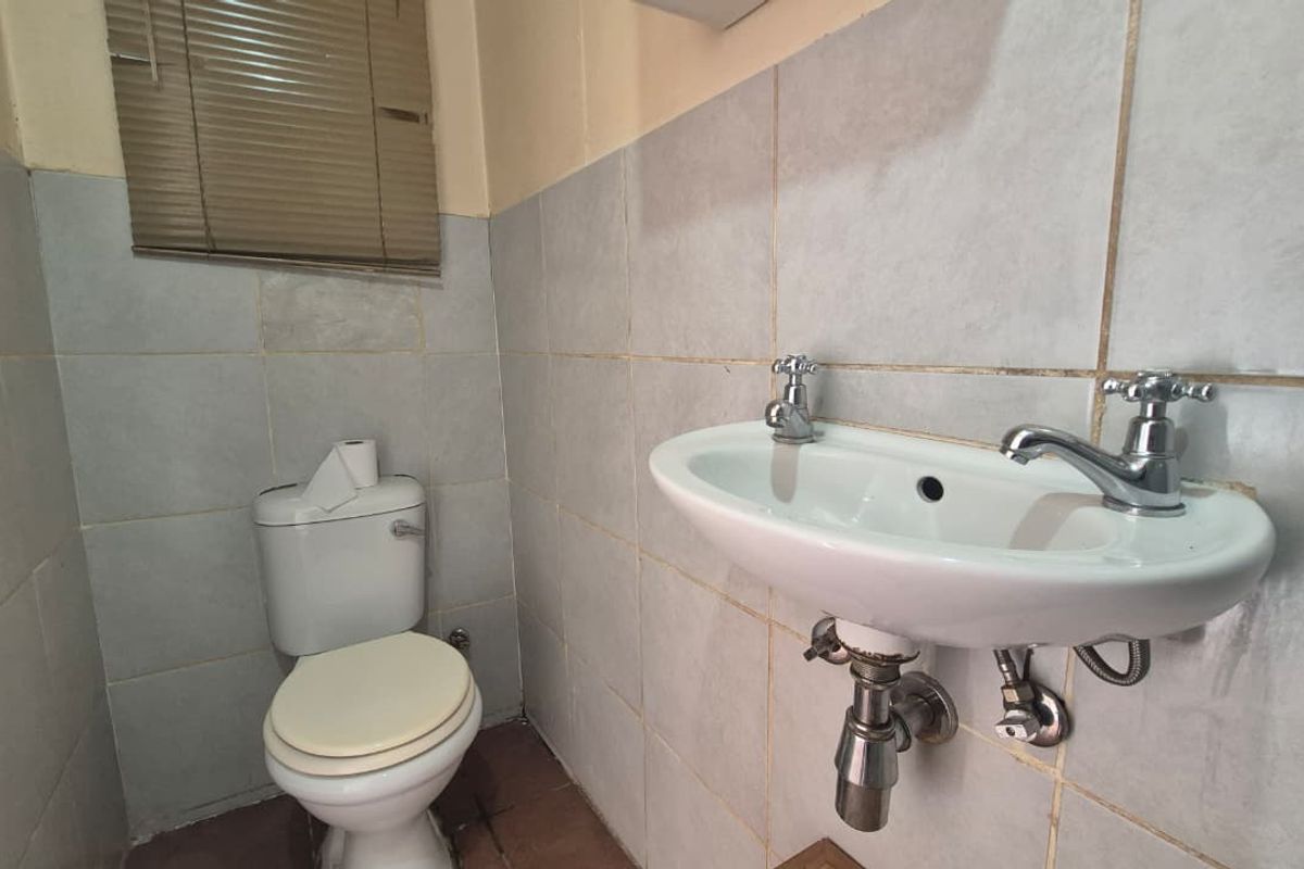 A compact bathroom featuring a wall-mounted basin and a standard ceramic toilet, finished with tiled walls and a window blind.