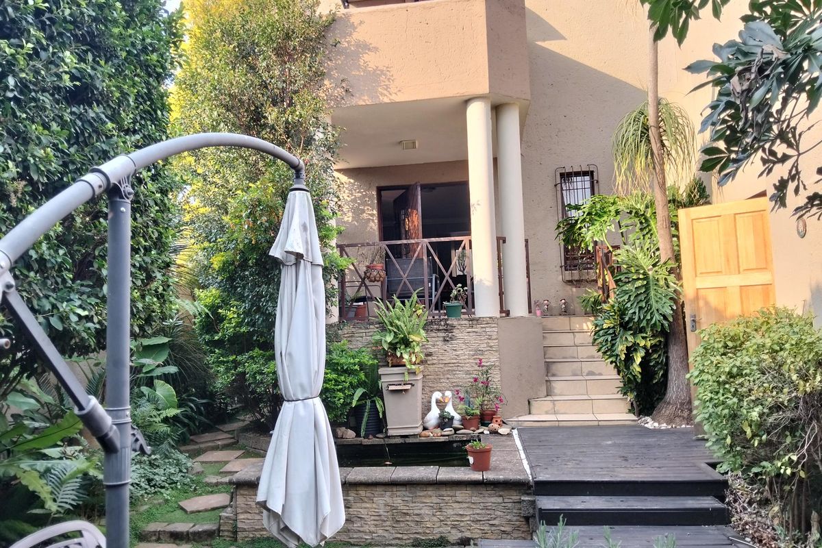 Rear view of the property featuring a landscaped garden, stone-clad water feature, timber decking, and a raised balcony with structural columns.