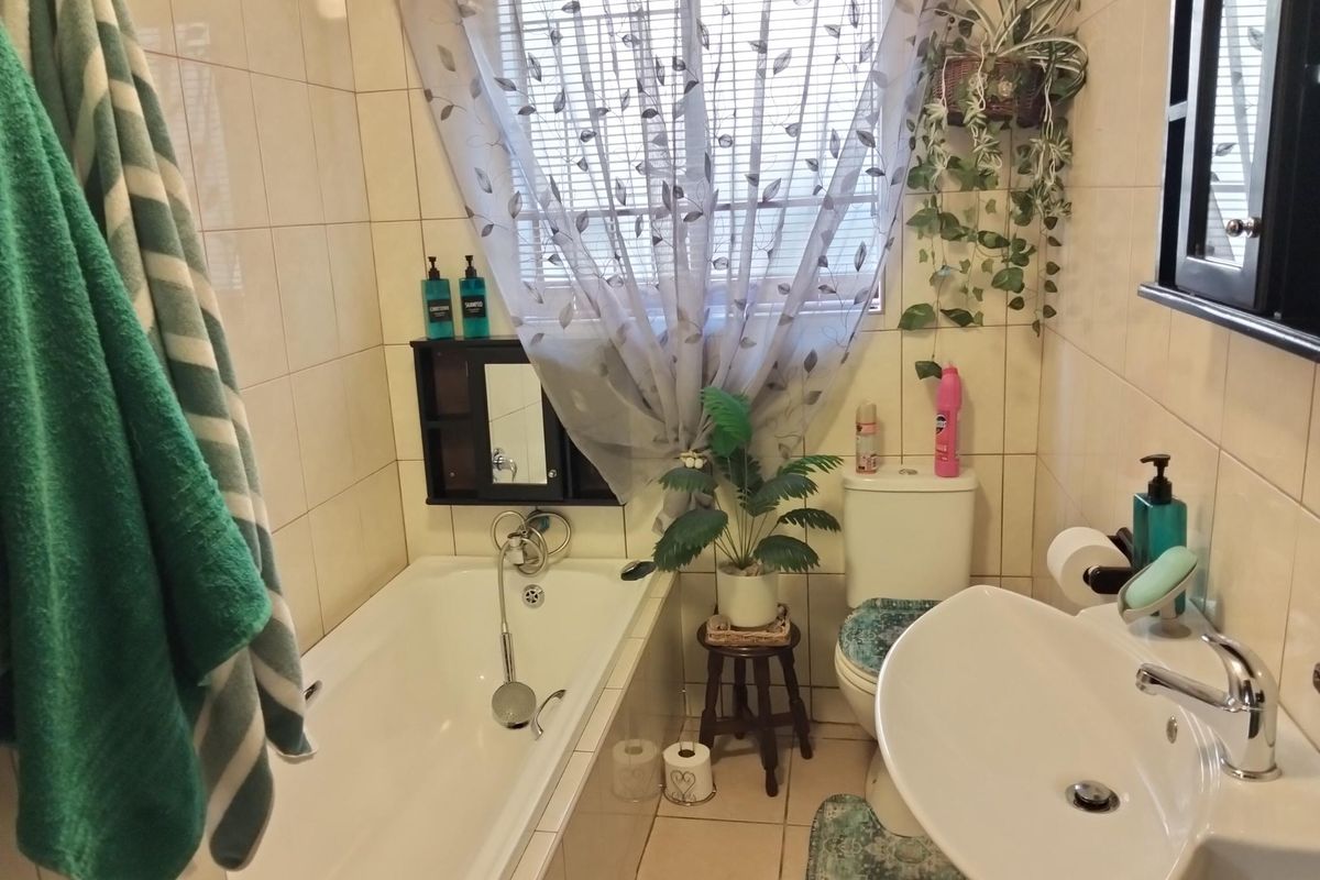A functional bathroom featuring a bathtub, pedestal basin, and toilet with neutral wall and floor tiling.