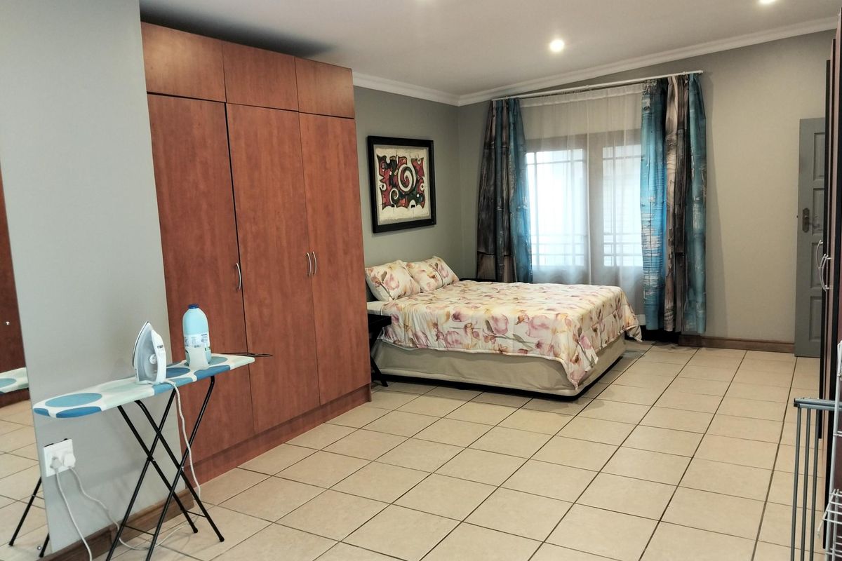 Spacious bedroom featuring neutral tiled flooring, built-in wooden cupboards, and recessed downlighting, offering a clean and functional living space.