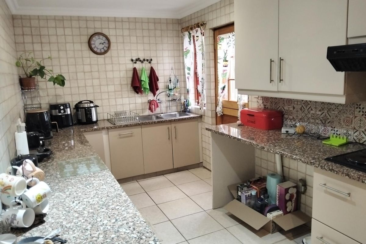 A functional kitchen featuring granite countertops, double bowl sink, built-in cabinetry, and an extractor fan, with ceramic tile finishes throughout.