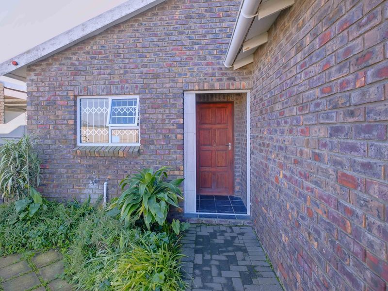 Front entrance of a face brick house featuring a timber door, security-barred window, and paved walkway access.