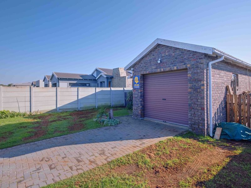A detached brick garage with a roller door, featuring a paved driveway and enclosed by a precast concrete boundary wall.