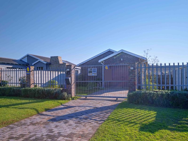 Front view of a brick house featuring a paved driveway, secure metal gate, and perimeter fencing.