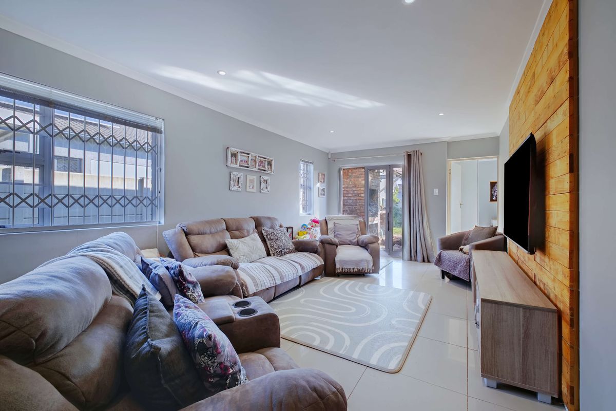 A bright living room featuring tiled floors, recessed lighting, a timber feature wall, and direct access to the outdoor area through sliding glass doors.