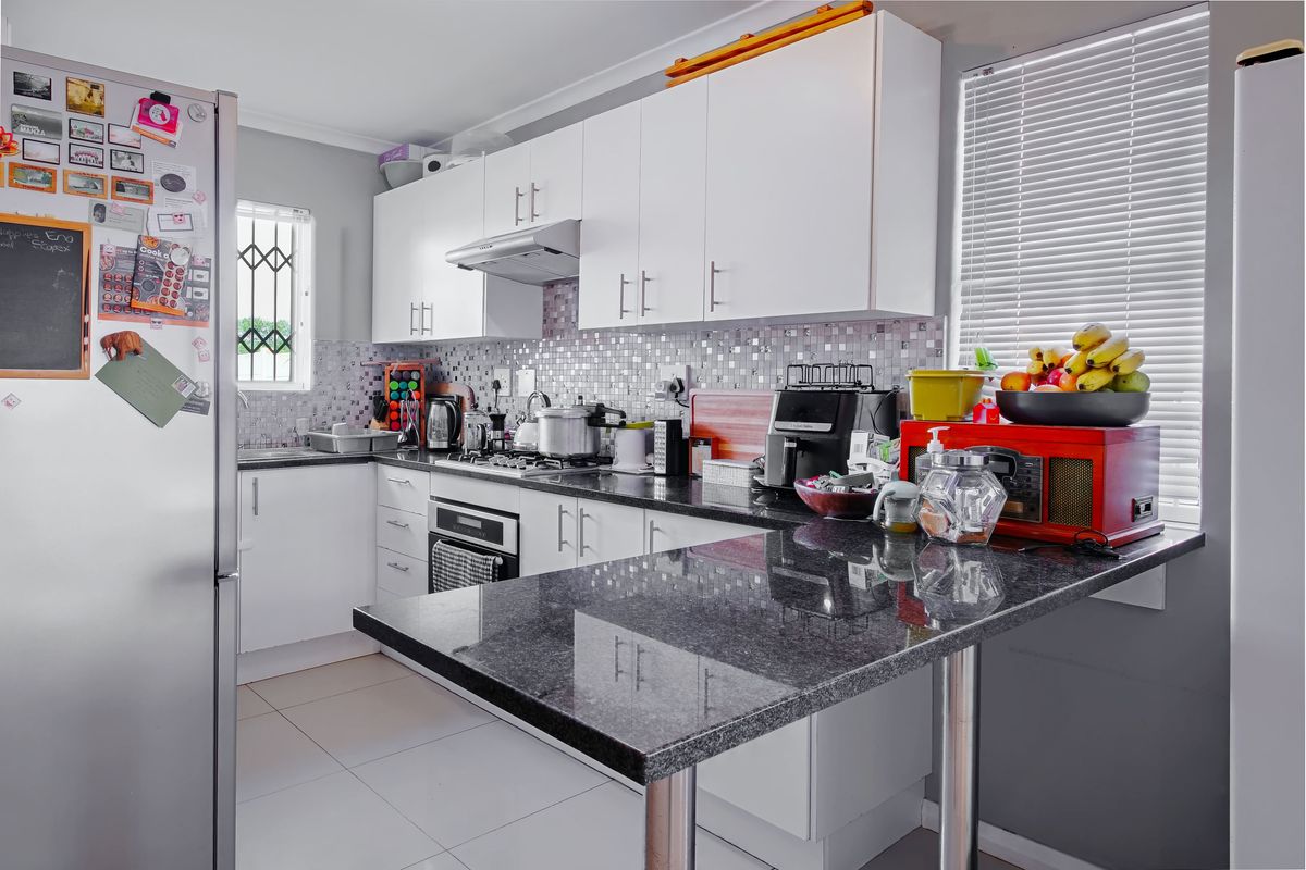 A functional kitchen featuring white cabinetry, granite countertops, a breakfast bar, and a mosaic tile backsplash with integrated oven and hob.