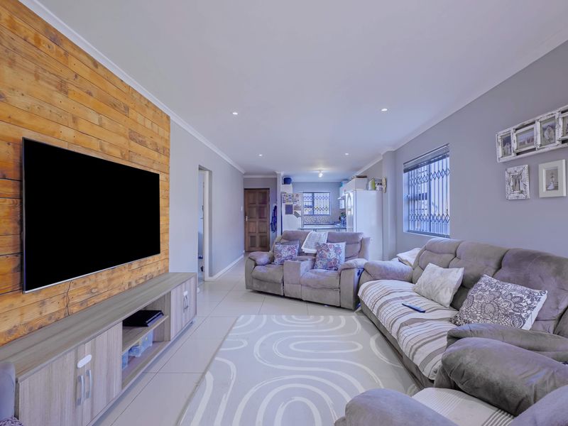 Open-plan living area featuring a timber accent wall, tiled flooring, and recessed downlighting, flowing into the kitchen space.