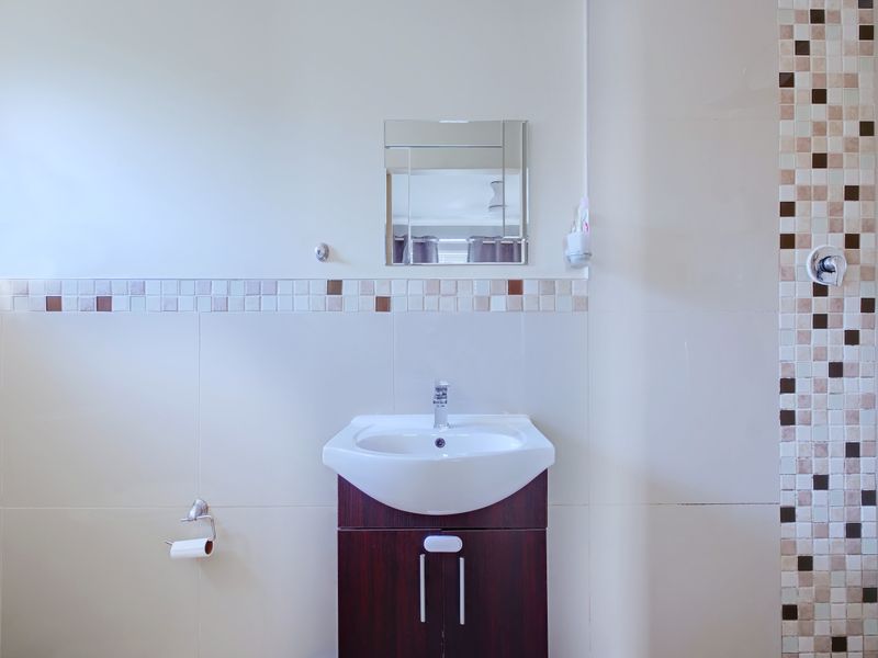 A clean bathroom featuring a dark wood vanity cabinet, ceramic basin, wall-mounted mirror, and decorative mosaic tile accents.