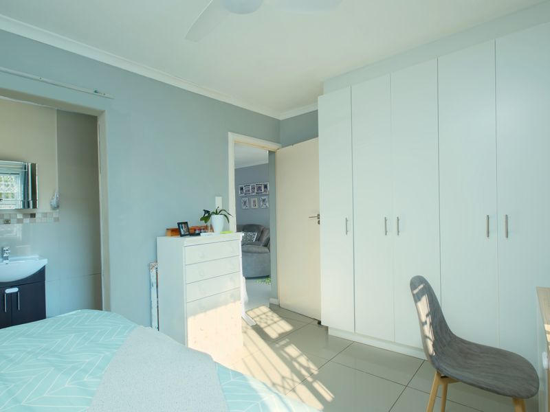 A well-maintained bedroom featuring built-in cupboards, tiled flooring, a ceiling fan, and an attached en-suite bathroom.