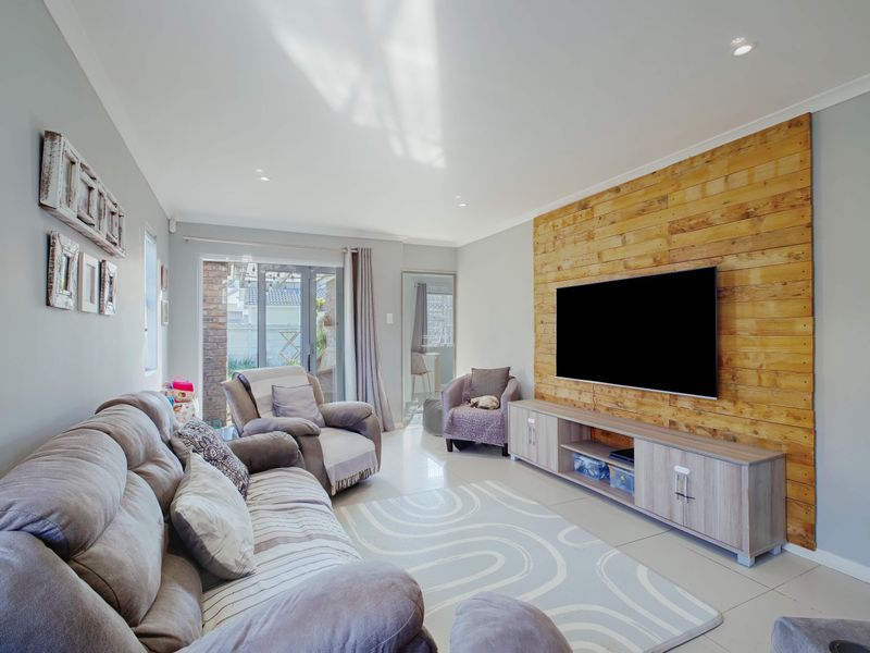 A bright living room featuring a timber accent wall, tiled flooring, recessed lighting, and direct access to an outdoor patio area.