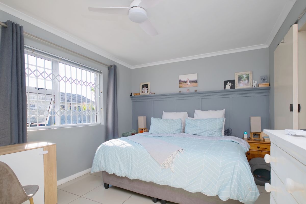 A well-maintained bedroom featuring neutral wall tones, tiled flooring, a ceiling fan, and a decorative built-in headboard panel.