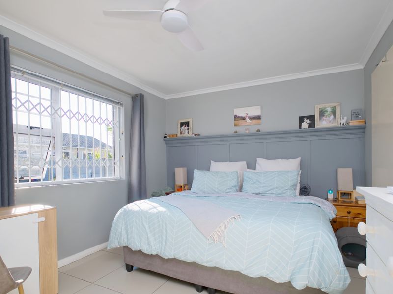 A well-maintained bedroom featuring neutral wall tones, tiled flooring, a ceiling fan, and a decorative built-in headboard panel.