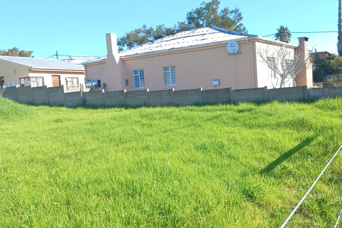 A view of a vacant residential plot featuring a grass lawn, enclosed by a precast concrete boundary wall and wire fencing.