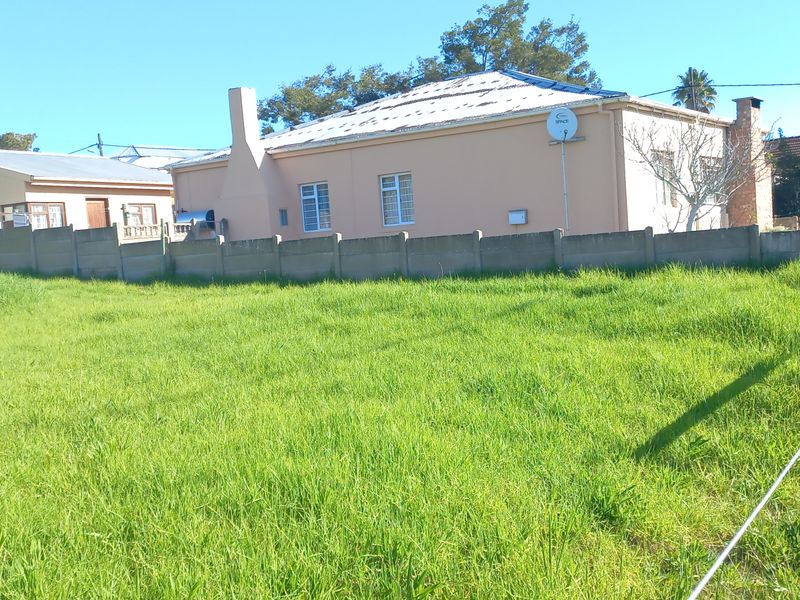 A view of a vacant residential plot featuring a grass lawn, enclosed by a precast concrete boundary wall and wire fencing.