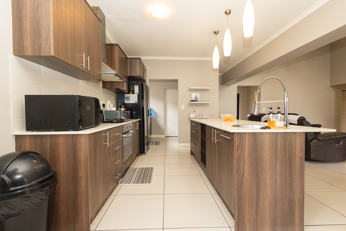 Modern kitchen featuring dark wood cabinetry, stone countertops, a central island with a prep sink, and integrated stainless steel appliances.