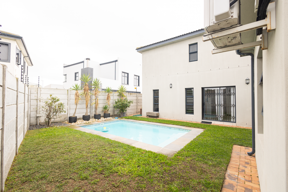 A private rear garden featuring a swimming pool, paved walkway, and perimeter walling, adjacent to the main house structure.