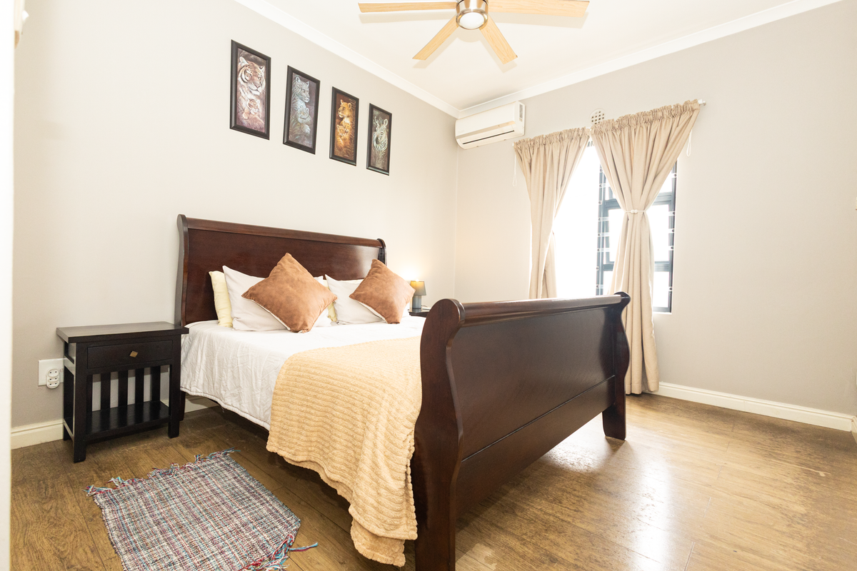 A well-maintained bedroom featuring wood-look flooring, a ceiling fan, and a wall-mounted air conditioning unit.