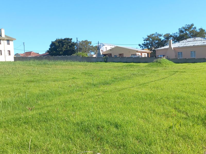 A vacant residential plot of land featuring a grass lawn and perimeter fencing, situated in a developed neighborhood.
