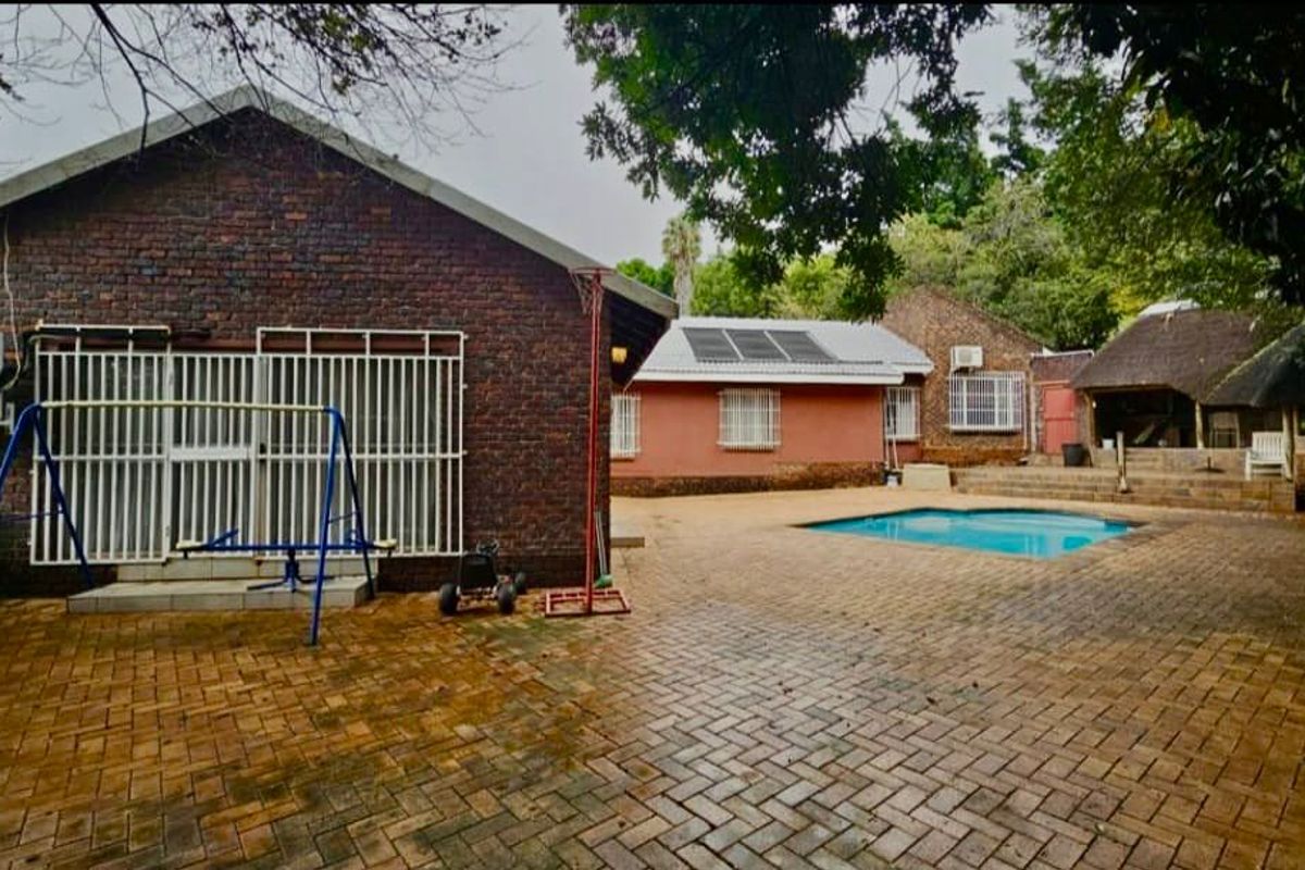 Rear exterior view featuring a paved courtyard, swimming pool, brick building facade, and a thatched lapa area.