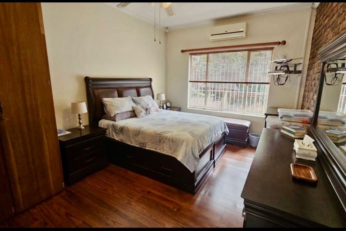 A well-maintained bedroom featuring laminate flooring, an exposed brick feature wall, built-in cupboards, and a split-system air conditioner.