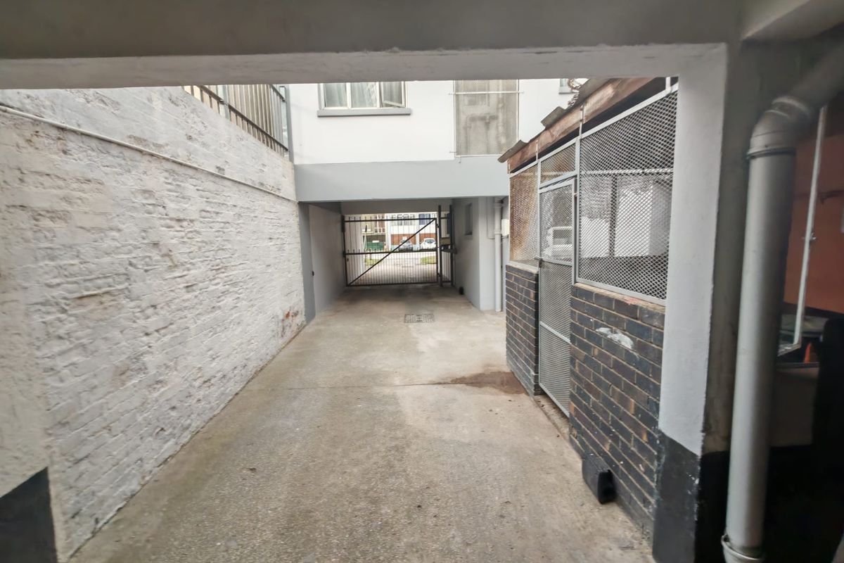 A rear exterior service area featuring a concrete driveway, brick boundary walls, and a secure metal gate leading to the street.