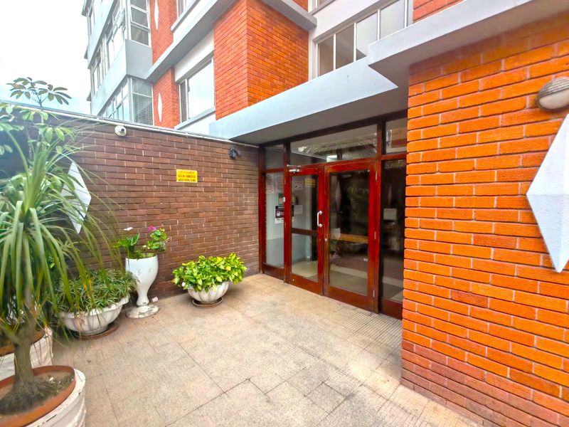 The apartment building entrance features a brick facade, glass double doors, and tiled flooring, providing a functional and secure access point to the property.
