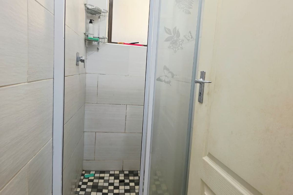 A compact shower cubicle featuring tiled walls, a checkered floor pattern, and a frosted glass door.