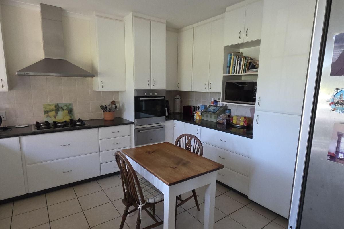 A functional kitchen featuring white cabinetry, dark countertops, a built-in oven, gas hob, and stainless steel extractor fan.