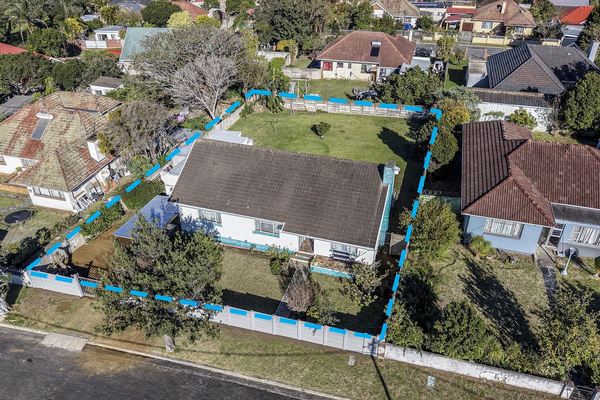 Aerial view of a residential property featuring a tiled roof house, surrounding garden, and perimeter wall boundary in a suburban neighborhood.
