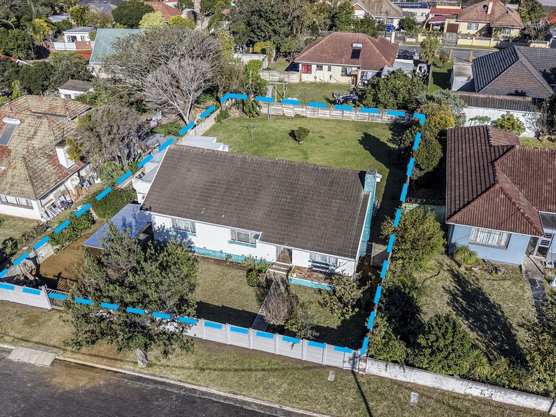 Aerial view of a residential property featuring a tiled roof house, surrounding garden, and perimeter wall boundary in a suburban neighborhood.
