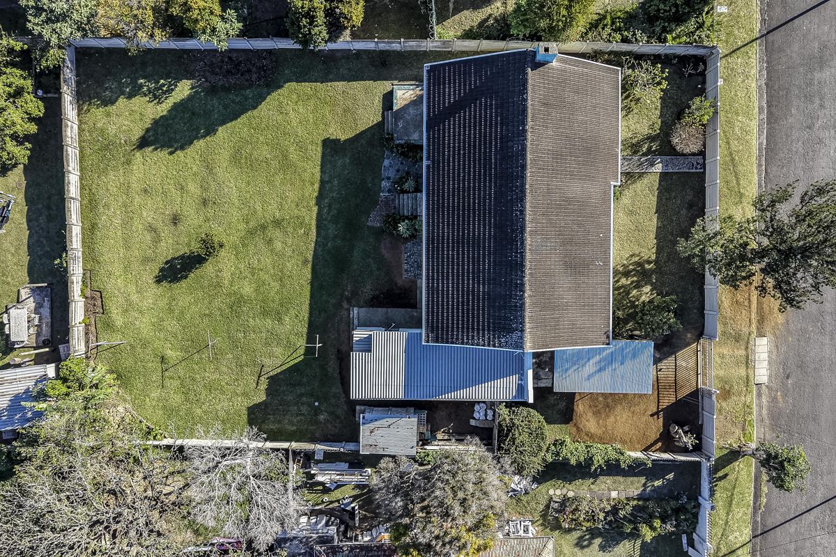 An aerial view of the property showing the main house with tiled and metal roofing, a large garden, and perimeter fencing.