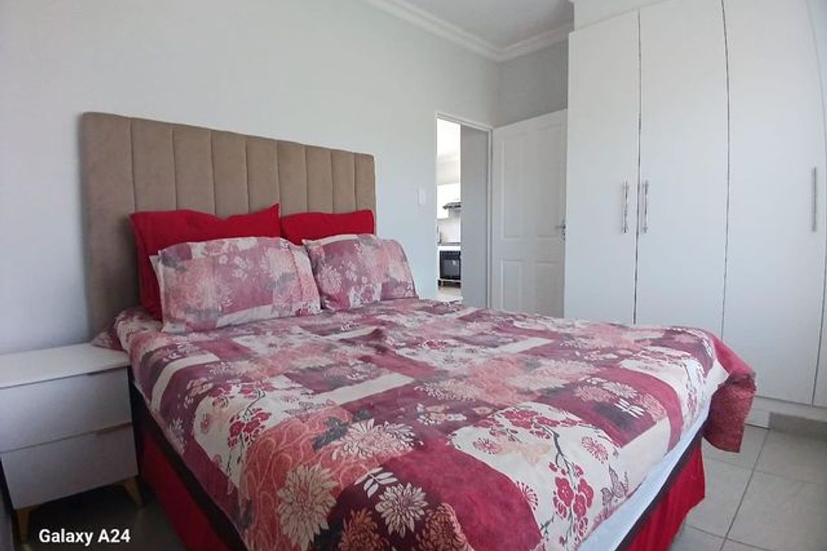 A well-maintained bedroom featuring built-in cupboards, tiled flooring, and neutral wall finishes, with a view into an adjacent room.