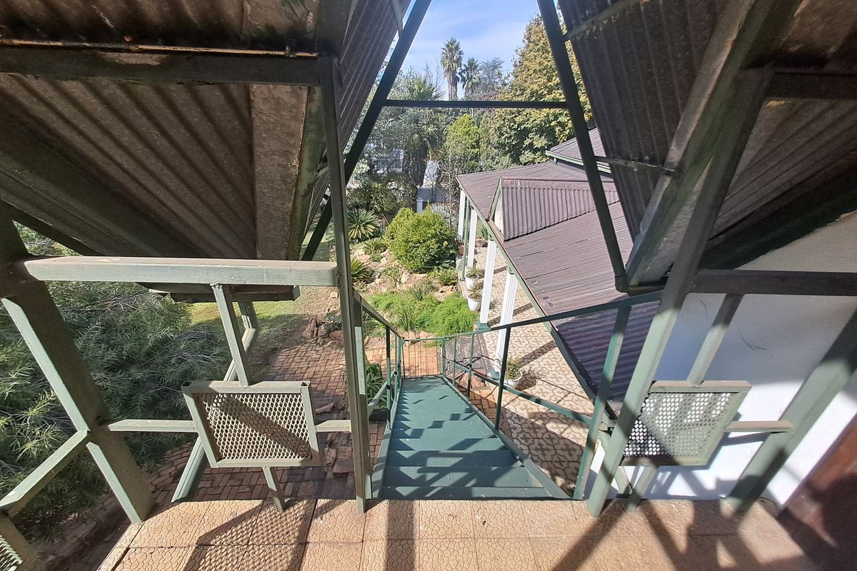 An elevated view looking down a metal staircase towards a paved rear patio and landscaped garden area.