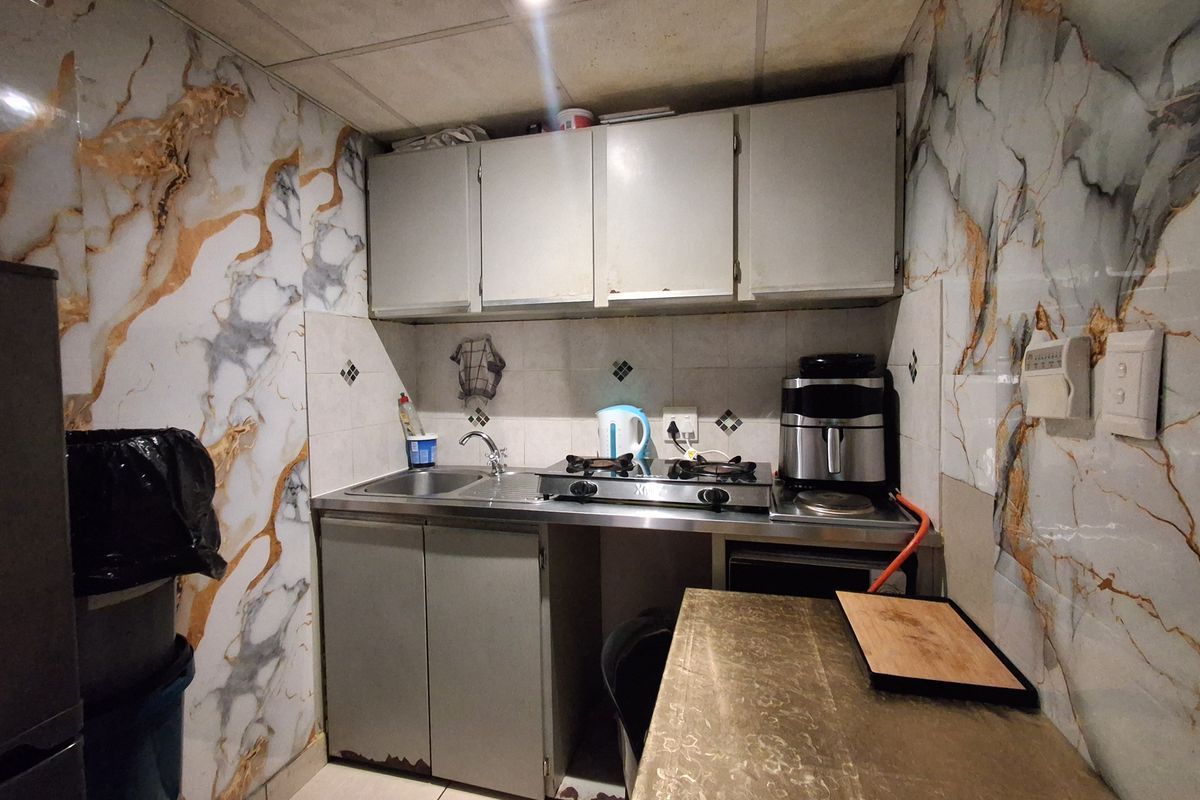 Compact kitchen featuring built-in cabinetry, a stainless steel sink, gas hob, and decorative marble-effect wall tiling.
