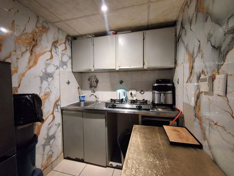 Compact kitchen featuring built-in cabinetry, a stainless steel sink, gas hob, and decorative marble-effect wall tiling.