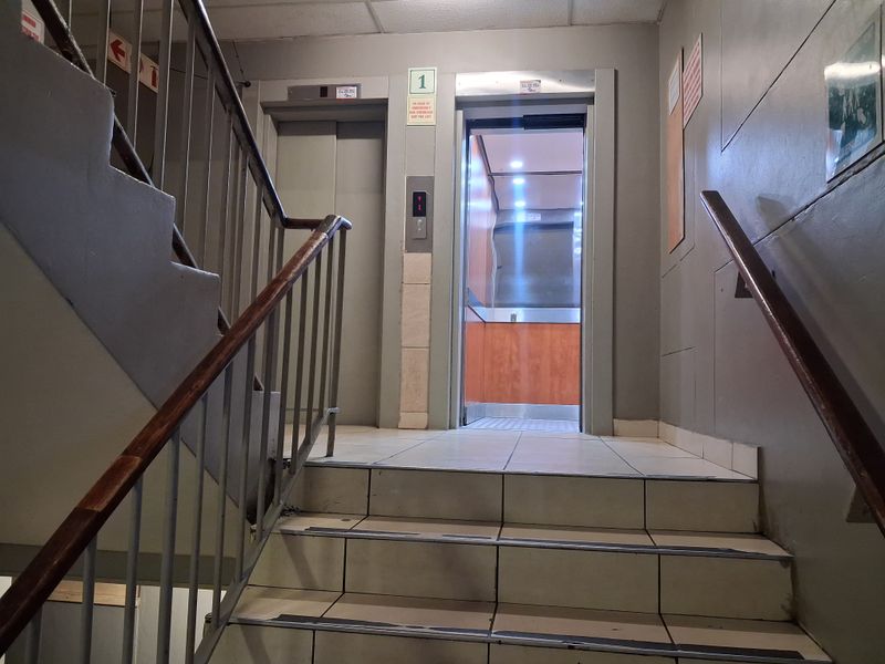A communal apartment hallway featuring a functional elevator, tiled staircase, and metal handrails, providing access to residential levels.